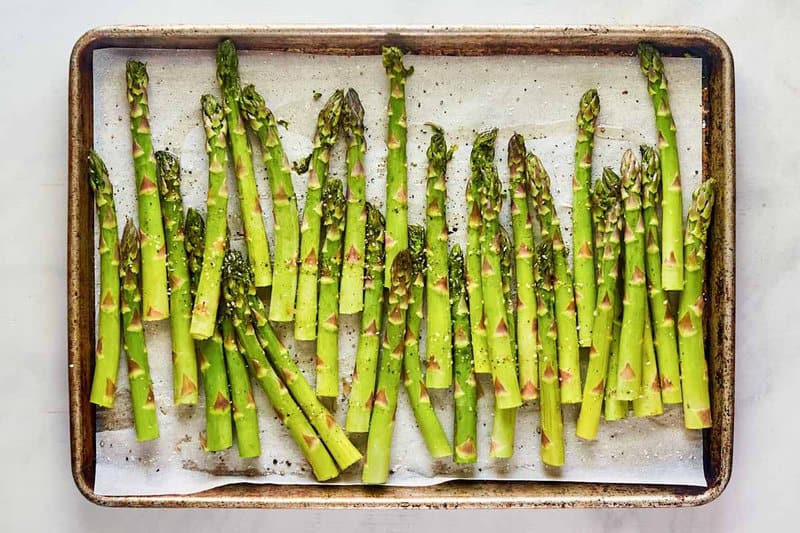 Seasoned asparagus spears on a baking sheet pan.