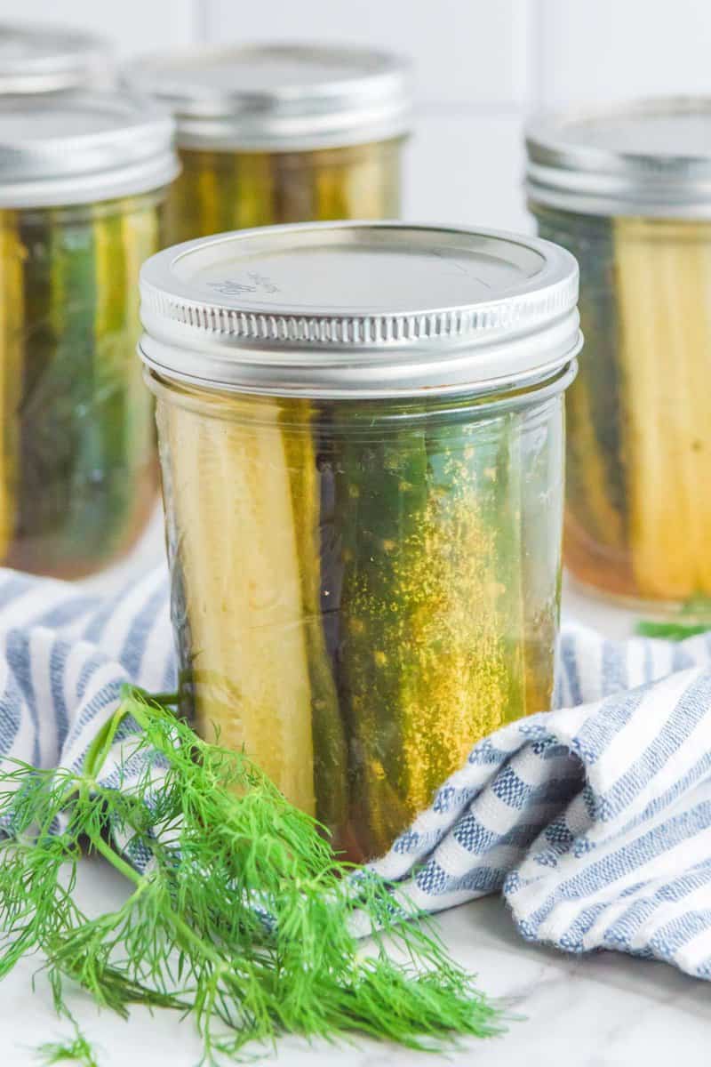 Homemade spicy dill pickles in a mason jar and fresh dill beside it.