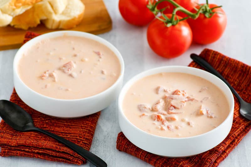 Copycat 4B's creamy tomato soup in two bowls, tomatoes, and bread slices.