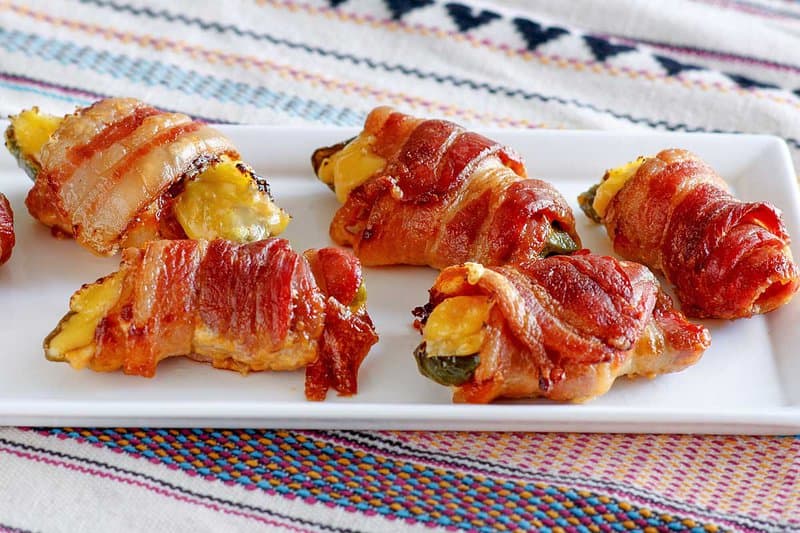Several air fryer bacon wrapped jalapeno poppers on a platter.