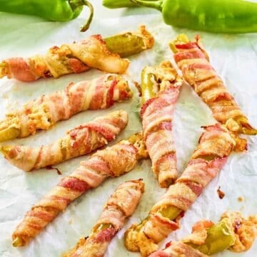 Bacon wrapped stuffed hatch peppers scattered on parchment paper.