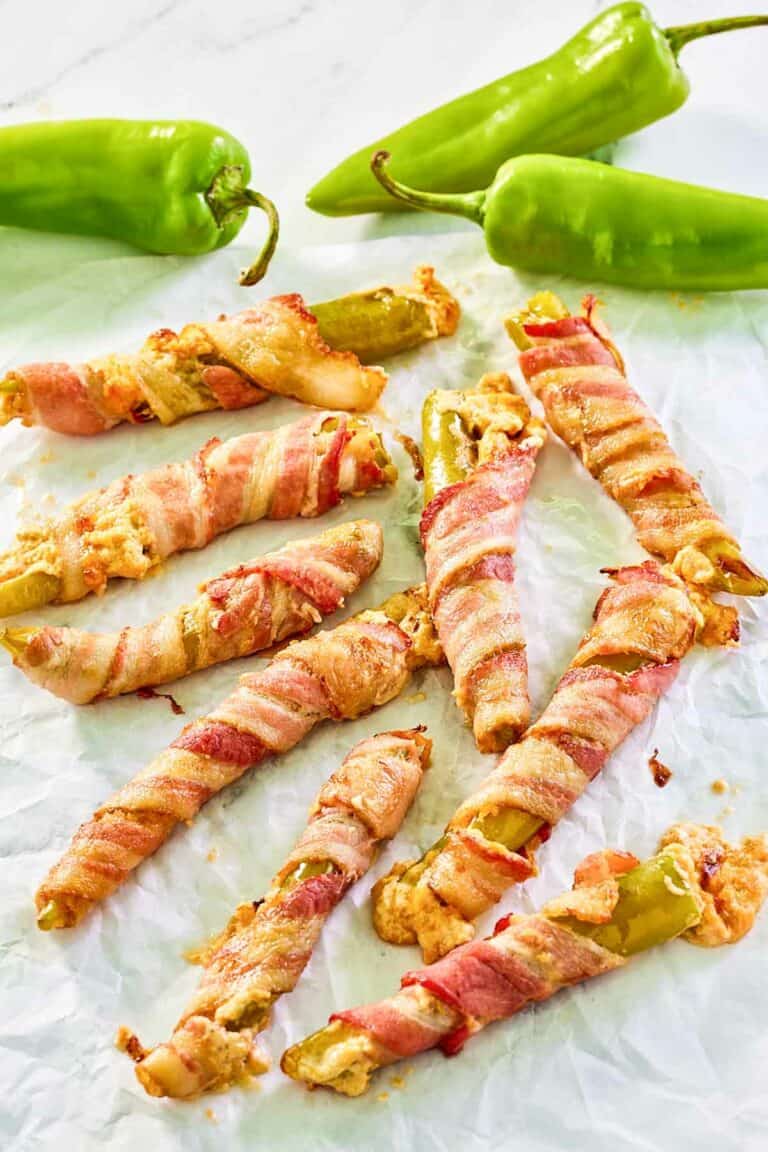 Bacon wrapped stuffed hatch peppers scattered on parchment paper.