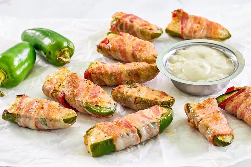 Bacon wrapped buffalo chicken poppers and dipping sauce on parchment paper.