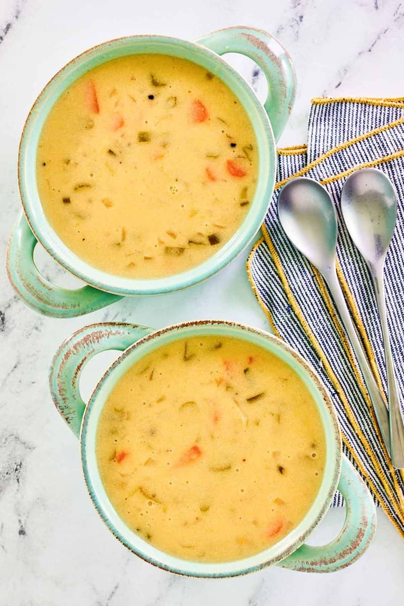 Overhead view of homemade cheddar cheese soup in soup crocks and two spoons.