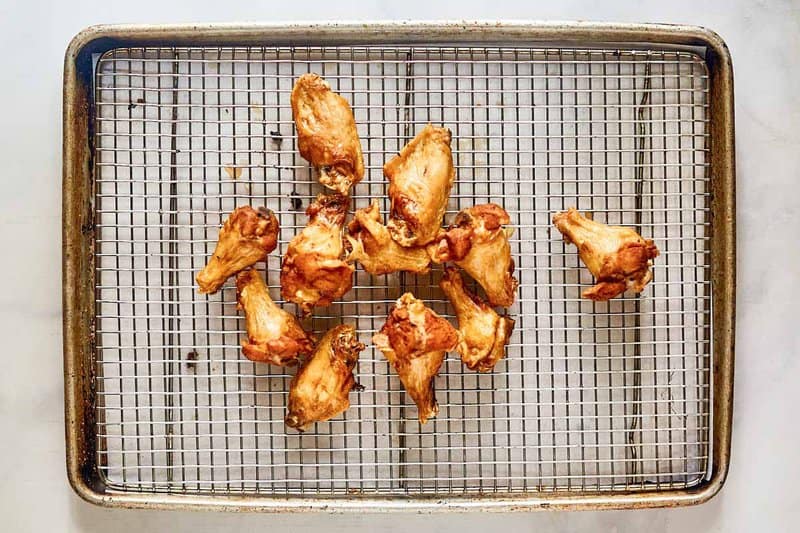 Fried chicken wings draining on a wire rack.
