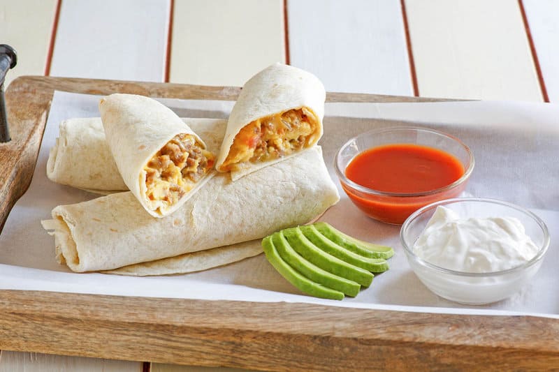 Copycat McDonald's breakfast burrito on a tray with avocado slices, salsa, and sour cream.