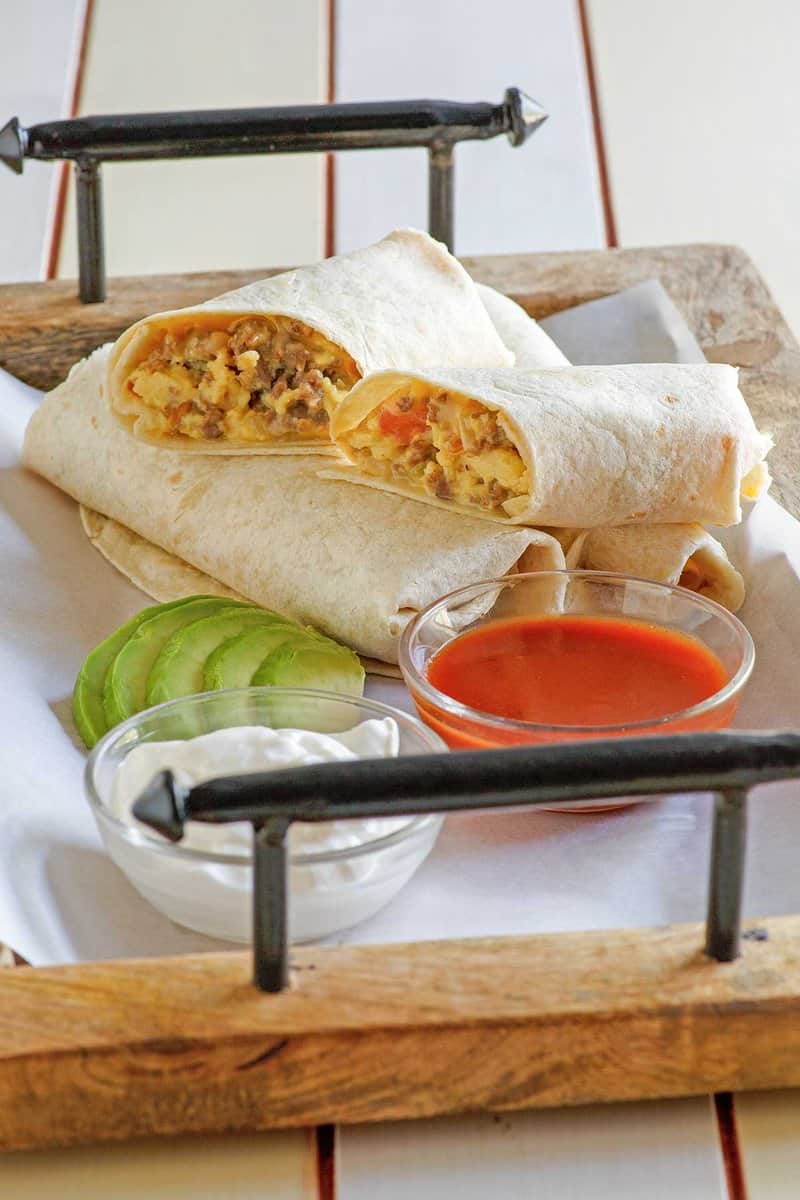 Copycat McDonald's breakfast burrito on a tray with sour cream, salsa, and avocado.