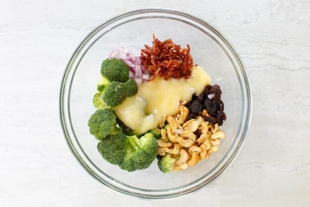 Adding dressing to broccoli salad ingredients in a bowl.