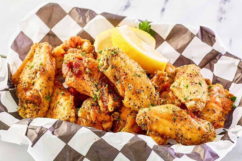 Copycat Buffalo Wild Wings lemon pepper wings and lemon wedges in a serving basket.