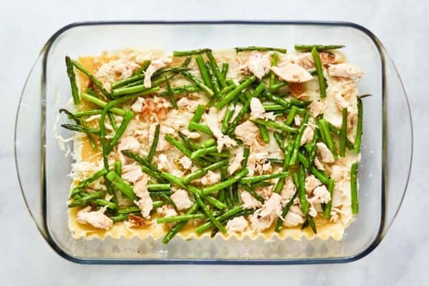 Chopped chicken and asparagus over lasagna noodles in a baking dish.
