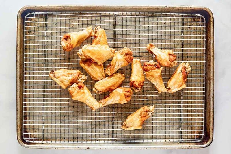 Deep fried chicken wings draining on a wire rack over a baking sheet.