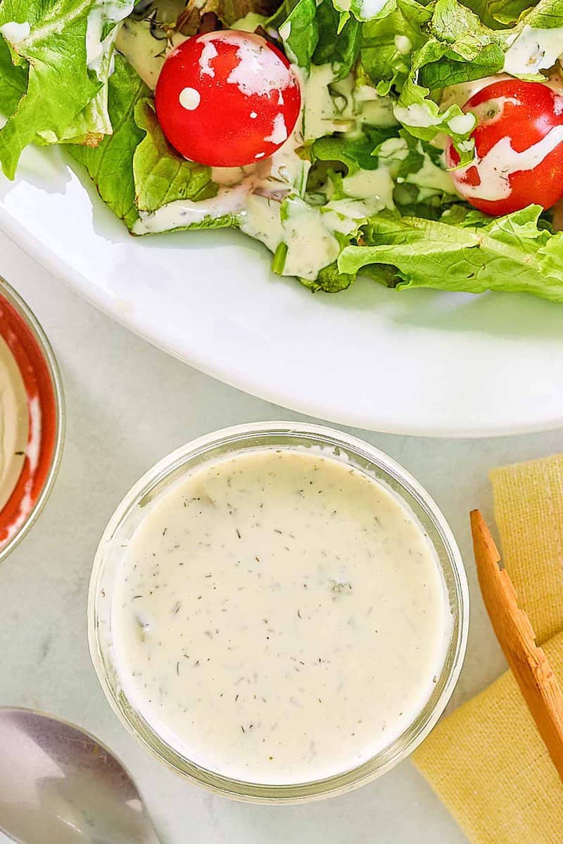 Overhead view of dill pickle ranch dressing on a salad and in a glass jar.