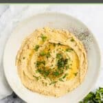 Overhead view of homemade garlic hummus topped with olive oil and fresh parsley.