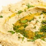 Closeup of homemade garlic hummus topped with olive oil and fresh herbs.