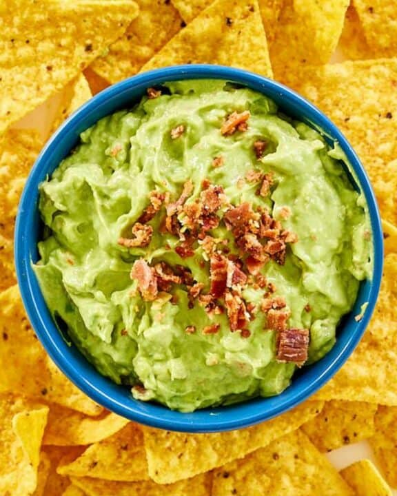 A bowl of avocado dip with bacon bits on top.
