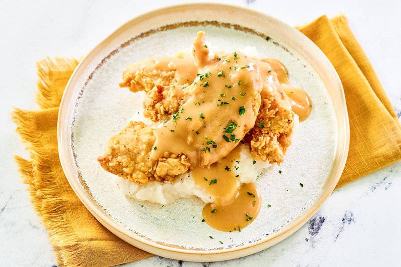 Copycat Cracker Barrel fried chicken tenders over mashed potatoes and topped with gravy.