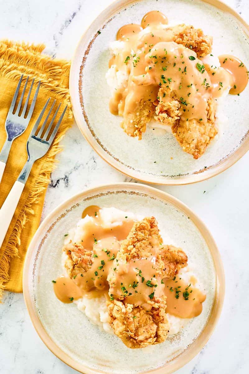 Copycat Cracker Barrel fried chickenhearted  tenders, mashed potatoes, and gravy connected  2  plates.