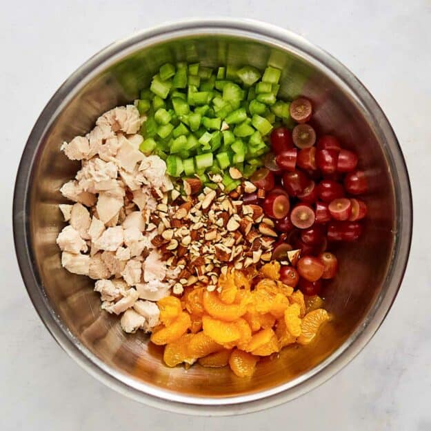 Chopped chicken, celery, grapes, mandarin oranges, and nuts in a mixing bowl.