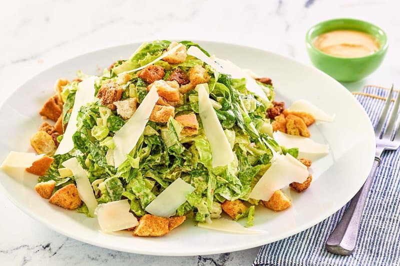 Copycat Houston's spicy Caesar salad on a plate and a bowl of spicy Caesar dressing.