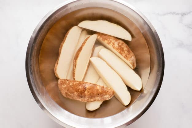 Russet potato wedges and water in a bowl.