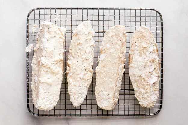 Battered potato wedges on a wire rack.