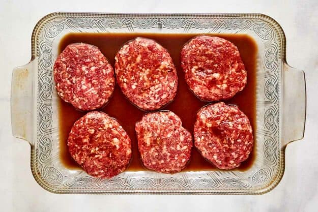 Oval sausage patties and beef broth in a baking dish.