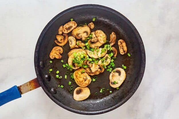 Sauteed mushrooms and scallions in a skillet.