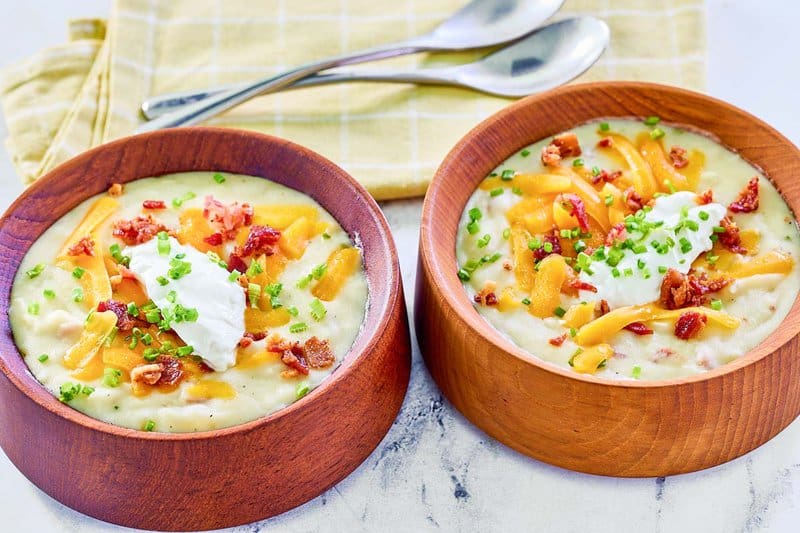 Copycat Panera baked potato soup in two bowls and two spoons behind them.