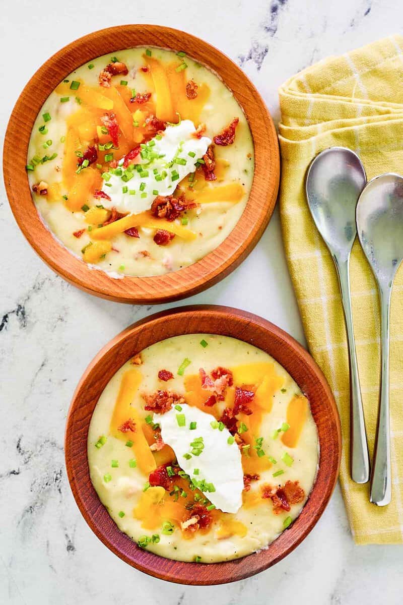 Two bowls of copycat Panera baked potato soup and two spoons on a reticulum napkin.