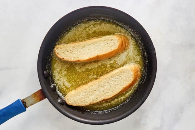 Dipping bread slices in garlic butter in a skillet.