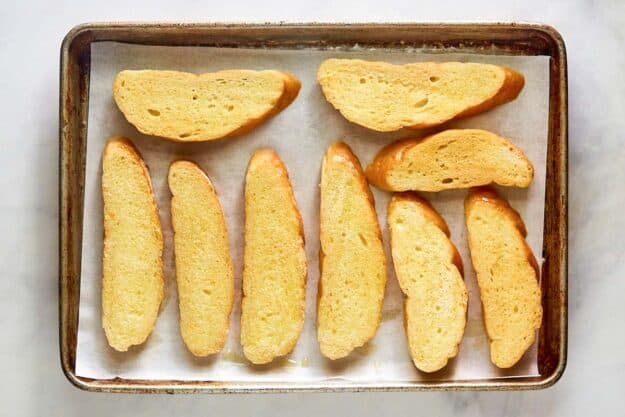 Bread slices with garlic butter on a baking sheet.