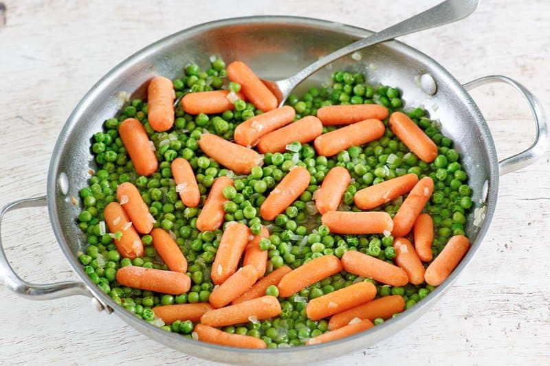 Buttery peas and carrots and a metal spoon in a skillet.