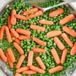 Buttery peas and carrots and a spoon in a skillet.