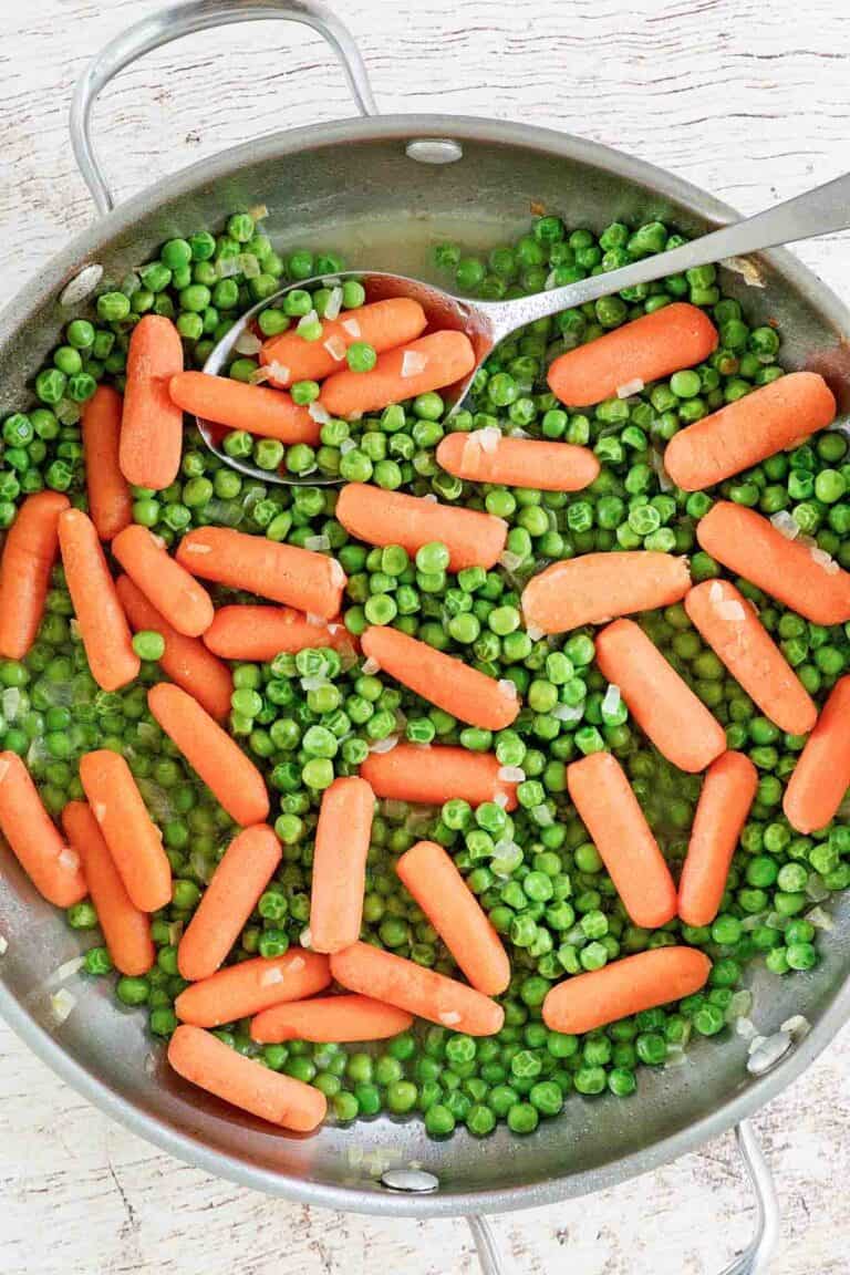Buttery peas and carrots and a spoon in a skillet.
