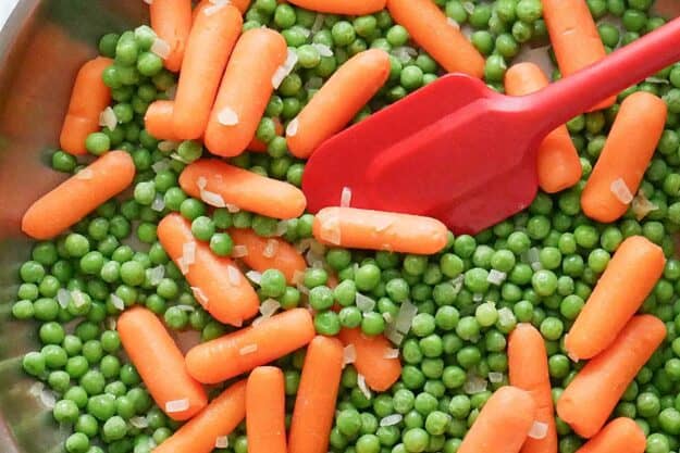 Buttery peas and carrots and a spatula in a skillet.