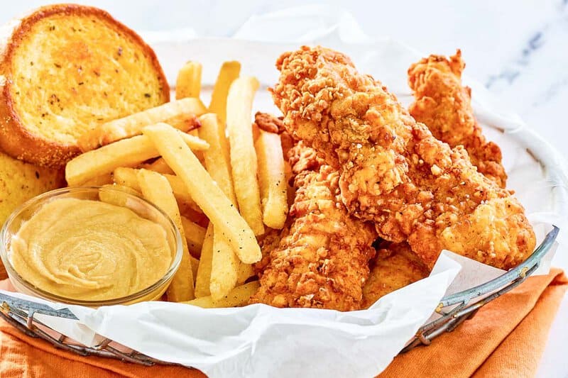 Copycat Whataburger chicken strips, fries, honey mustard sauce, and toast in a basket.