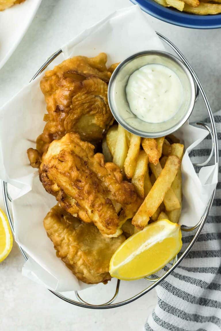 Beer battered fish and chips, lemon wedge, and a cup of tartar sauce in a serving basket.