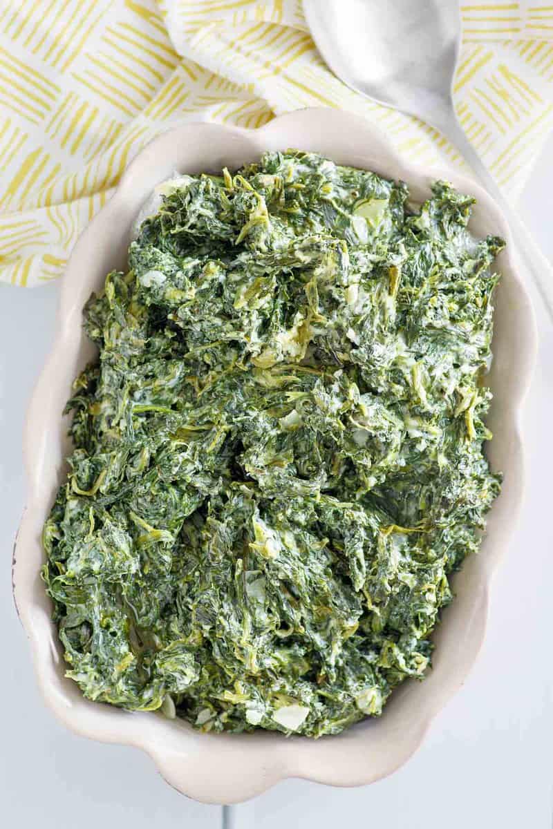 Copycat Boston Market creamed spinach in a baking dish and a serving spoon next to it.