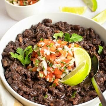 Copycat Chili's black beans garnished with pice de gallo and lime wedges.