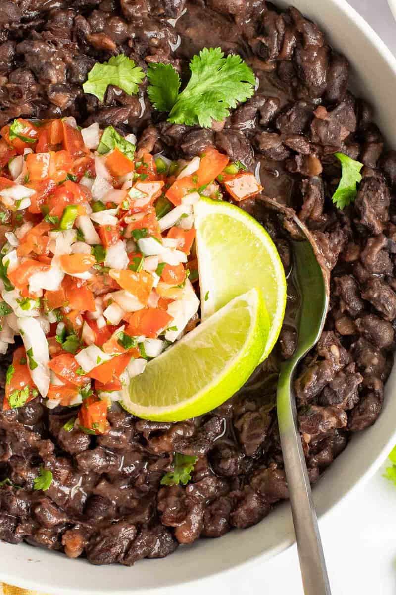 A bowl of copycat Chili's black beans with pico de gallo and lime wedges on top.
