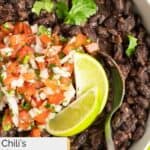 A bowl of homemade Chili's black beans topped with pico de gallo and lime wedges.