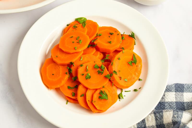 Cooked carrots topped with chopped fresh parsley on a plate.