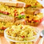 Curried chicken salad in a small glass bowl and sandwiches behind it.