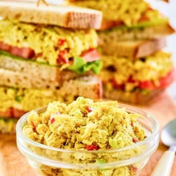 Curried chicken salad in a small glass bowl and sandwiches behind it.