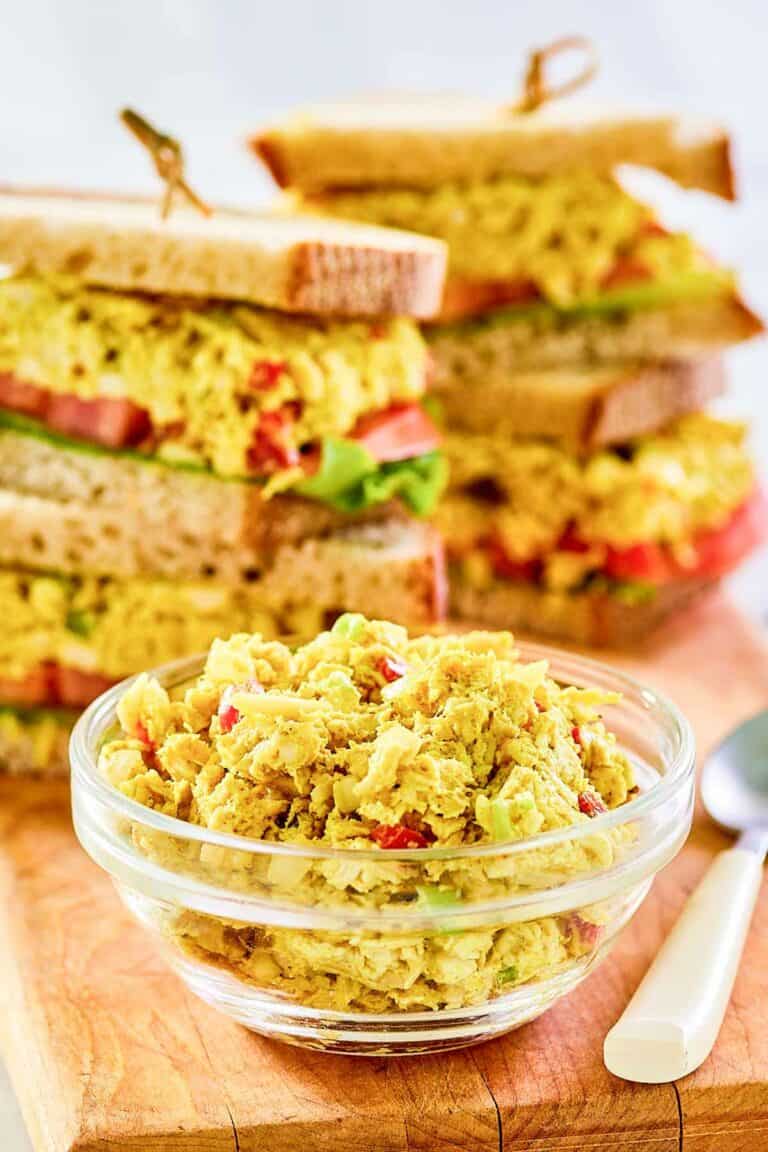Curried chicken salad in a small glass bowl and sandwiches behind it.
