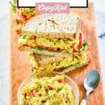 A bowl of curried chicken salad and sandwiches on a wood board.