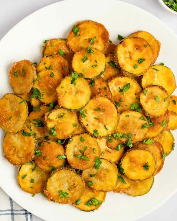 Fried zucchini garnished with parsley on a platter.