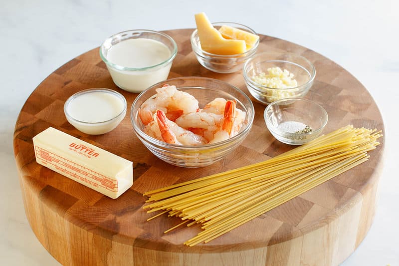 Copycat Olive Garden shrimp alfredo ingredients on a round wood board.