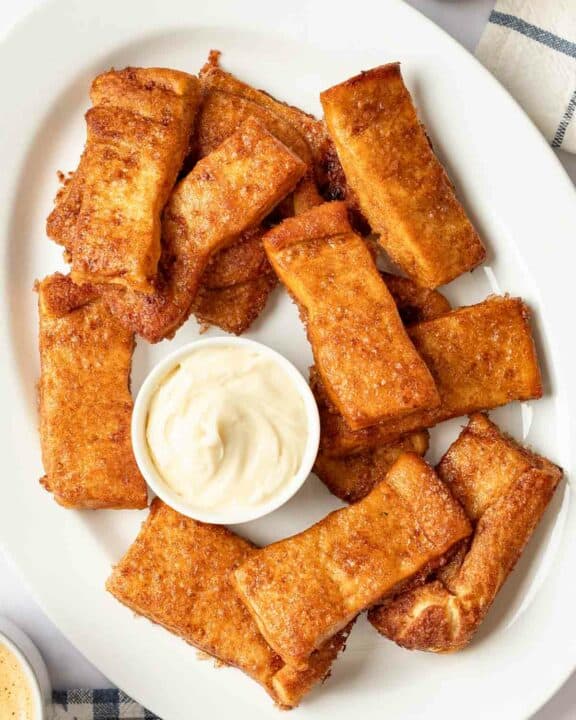 Copycat Pizza Hut Cinnamon Sticks and a bowl of cream cheese icing on a platter.