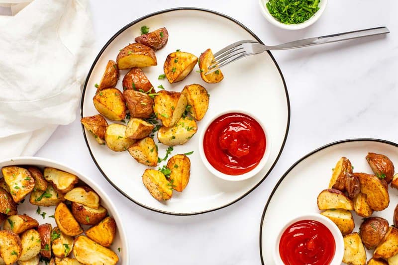 Roasted red potatoes and ketchup on plates.
